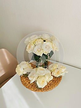 Beautiful bouquets of white roses in a glass vase on a white table and interior on a wicker placemat. Minimalistic