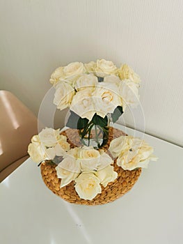 Beautiful bouquets of white roses in a glass vase on a white table and interior on a wicker placemat. Minimalistic