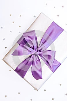 Beautiful box-gift in silver paper with trendy violet ribbon and bow-knot and sprickle stars. Holiday concept