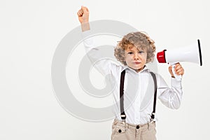 Beautiful boy with curly hair in white shirt, brown hat, glasses with black suspenders listening throung a megaphone