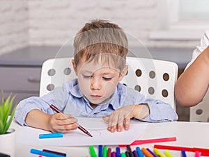 Beautiful boy drawing picture with pencil in class. Concentrated boy