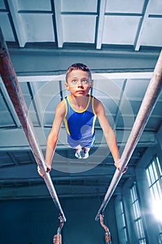 Beautiful boy is engaged in sports gymnastics on a parallel bars