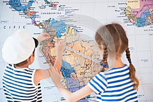 Beautiful boy and a girl in sailor striped shirts measure distance on world map with measuring tape