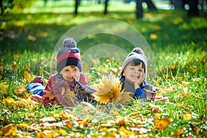 Beautiful boy, little child laying with a lot of yellow autumn leaves in park. Kid boy having fun on sunny warm october day.