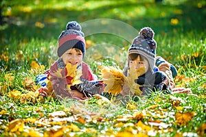 Beautiful boy, little child laying with a lot of yellow autumn leaves in park. Kid boy having fun on sunny warm october day. Seaso