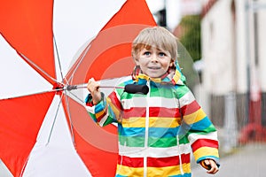 Beautiful boy with red umbrella and colorful jacket outdoors at