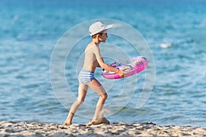 Beautiful boy running on sand with a life-buoy
