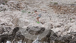 A beautiful boy walking on the beach of the Adriatic Sea and climbing high on the rock throwing sea stones in the water