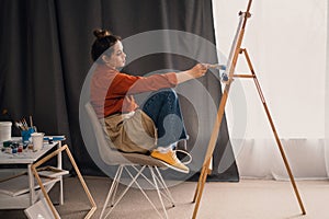 A beautiful Brazilian woman artist with paint on her hands works on painting a picture on canvas while sitting in front