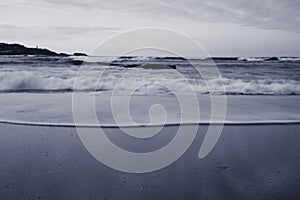 Beautiful breaking waves on sandy beach on atlantic ocean in black and white, hendaye, basque country,