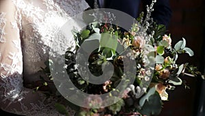 Beautiful bridal bouquet in hands of young bride dressed in white wedding dress. Bride hand touching the wedding bouquet