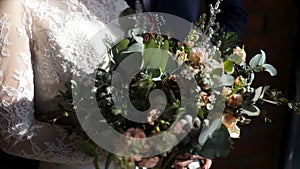 Beautiful bridal bouquet in hands of young bride dressed in white wedding dress. Bride hand touching the wedding bouquet