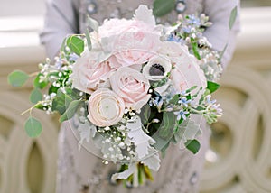 Beautiful bridal bouquet made of creamy and light pink peonies, roses, ranunculuses, baby breath and eucalyptus branches