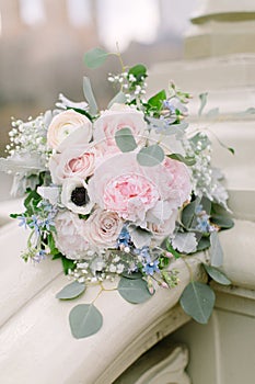 Beautiful bridal bouquet made of creamy and light pink peonies, roses, ranunculuses, baby breath and eucalyptus branches