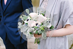 Beautiful bridal bouquet made of creamy and light pink peonies, roses, ranunculuses, baby breath and eucalyptus branches