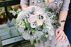 Beautiful bridal bouquet made of creamy and light pink peonies, roses, ranunculuses, baby breath and eucalyptus branches