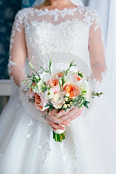 Beautiful bridal bouquet with white roses and peach peonies in a bride hands in white dress. Wedding morning. Close-up