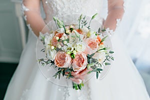 Beautiful bridal bouquet with white roses and peach peonies in a bride hands in white dress. Wedding morning. Close-up