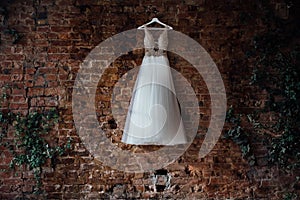 Beautiful bridal wedding dress hanging on a hanger on a brick wall in a loft studio. No one.