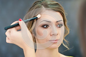 Beautiful bride applying wedding make-up in salon