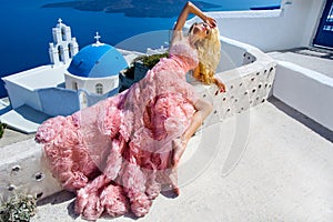 Beautiful bride blonde female model in amazing wedding dress poses on the island of Santorini in Greece