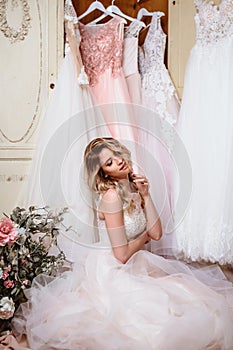 Beautiful bride blonde woman sitting near vintage wardrobe full of wedding dresses. fashion beauty portrait