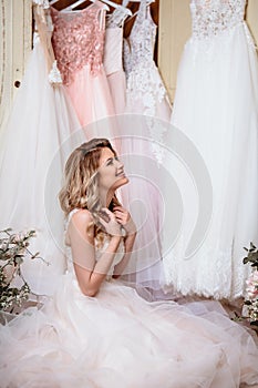 Beautiful bride blonde woman sitting near vintage wardrobe full of wedding dresses. fashion beauty portrait
