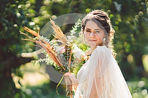 Beautiful bride with bouquet flowers stands on forest background. Rustic style. beautiful bride in delicate dress outdoors. Close