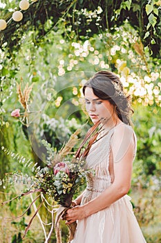 Beautiful bride with bouquet flowers stands on forest background. Rustic style. beautiful bride in delicate dress outdoors. Close