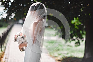 Beautiful bride in bridal gown with bouquet and lace veil on the nature. Beautiful model girl in a white wedding dress