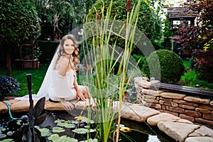 beautiful bride with curls near an artificial pond in a summer park.