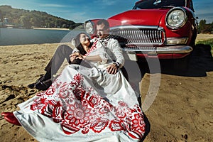 Beautiful bride and elegant stylish groom sitting near retro car with tender feelings, concept of love and life