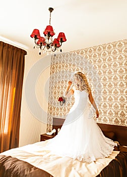 Beautiful bride with fashion veil posing on bed at wedding morning. Makeup. Blonde girl with long wavy hair styling