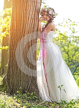 Beautiful bride , flower tiara on her head , relying on the tree