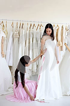 Beautiful bride getting dressed by her best friend in her wedding day and choosing a wedding dress in the shop and the shop