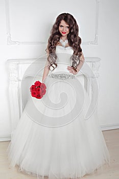 Beautiful bride girl with red roses bouquet posing in modern int