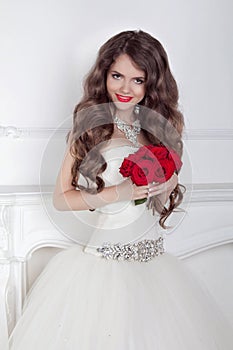 Beautiful bride girl with red roses bouquet posing in modern int