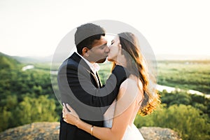Beautiful bride and groom embracing and kissing on their wedding day outdoors