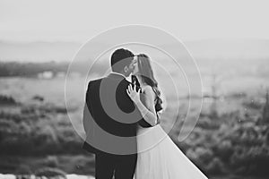 Beautiful bride and groom embracing and kissing on their wedding day outdoors