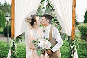 Beautiful bride and groom embracing and kissing on their wedding day outdoors