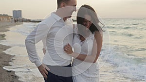 Beautiful bride and handsome groom are having fun on the beach during the sunset. They are hugging, running and tenderly