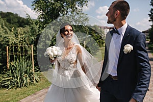 Beautiful bride with her handsome groom walking outside on theri wedding day. Happy newlyweds