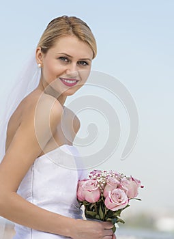Beautiful Bride Holding Flower Bouquet Against Clear Blue Sky