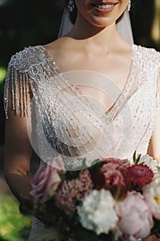 Beautiful bride is holding a wedding colorful bouquet in lace dress with beads. Beauty of colored flowers. Close-up. Bridal