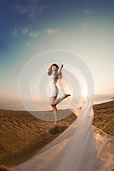 Beautiful bride with a long veil on the beach at sunset