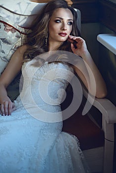 Beautiful bride in luxurious wedding dress with sweetheart neckline sitting ion the vintage sofa in relaxed pose