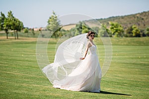Beautiful bride in luxury fashion white wedding dress with veil on the green golf club glade, wedding day. Amazing full