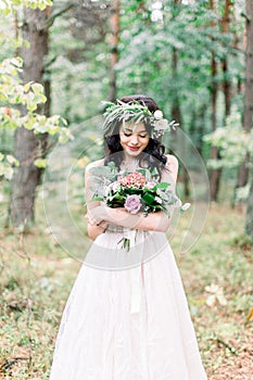 Beautiful bride in nature in a coniferous forest in a wreath on her head and a luxurious wedding dress. Rustic boho