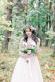 Beautiful bride in nature in a coniferous forest in a wreath on her head and a luxurious wedding dress. Rustic boho