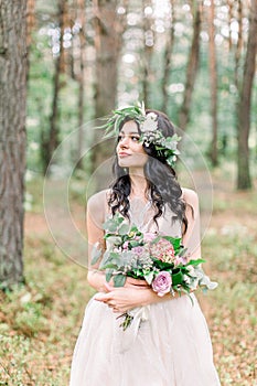 Beautiful bride in nature in a coniferous forest in a wreath on her head and a luxurious wedding dress. Rustic boho